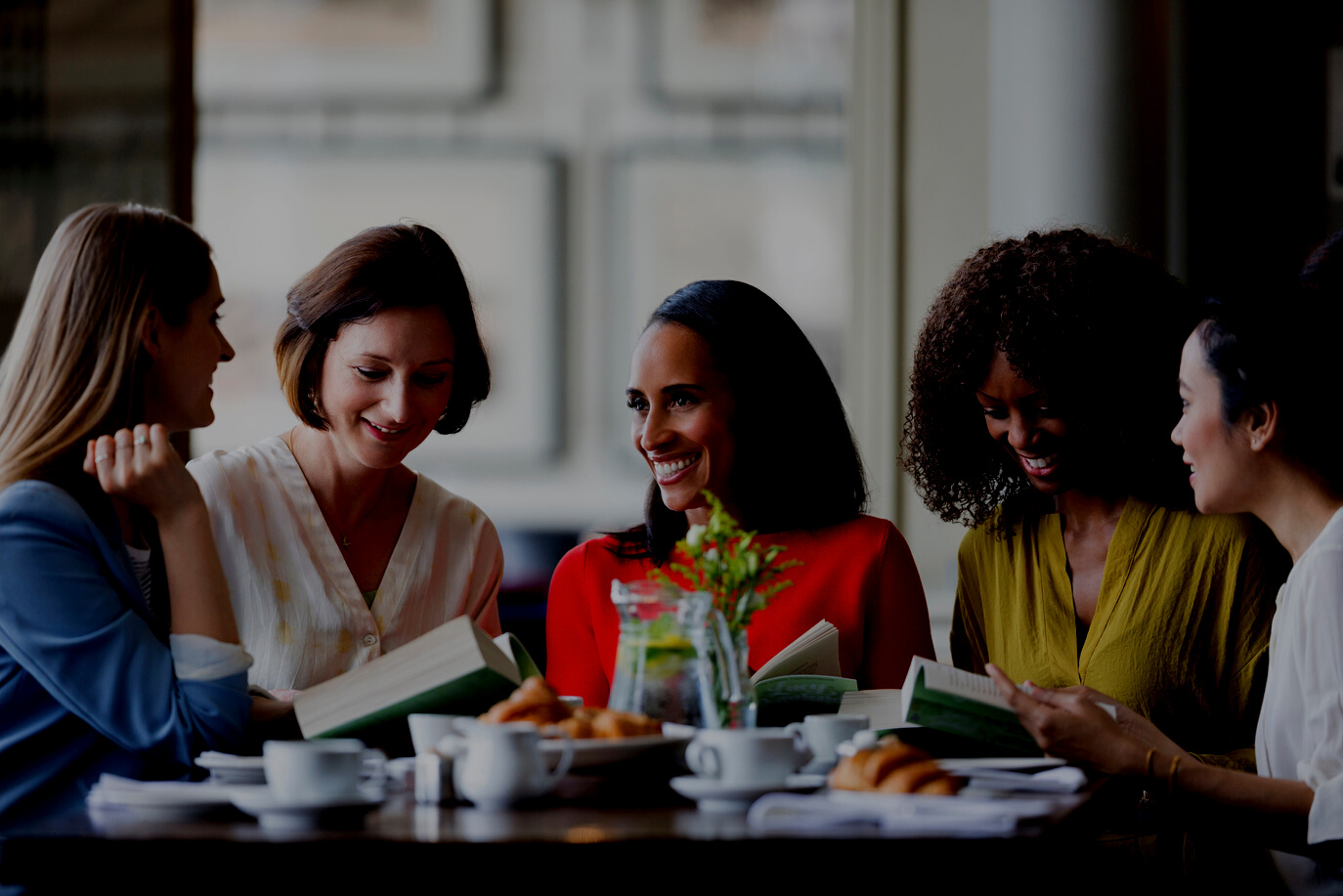 Women friends discussing book club book at restaurant table.